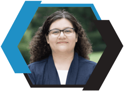 A woman with curly hair and glasses smiling outdoors, representing Braumiller Law Group.